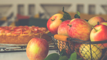 Ripe organic apples in vintage basket on rustic white table. Apple cheesecake in the background. Summer homemade apple tart with ingredients. Healthy organic food. Tasty breakfast.