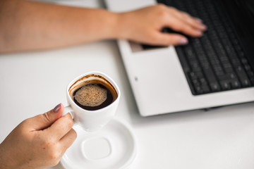 Coffee break at workplace. Woman typing on laptop and holding cup with hot drink. Eating habits, snacking, caffeine addiction, inspiration and morning routine