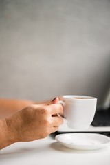 Cup of coffee at coffee shop table and and woman working on laptop. Typing female hands on keyboard. Morning routine at workplace