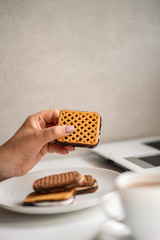 Unhealthy snack at workplace. Hands of woman working at computer and taking cookies from plate. Bad habits, junk food, high calorie eating, weight gain and lifestyle concept