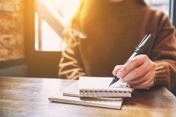 Closeup image of a woman writing on blank notebook with fountain pen on wooden table