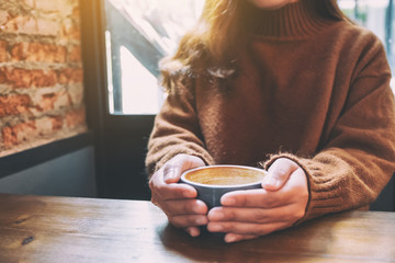 Closeup image of a woman holding a cup of hot coffee on wooden table