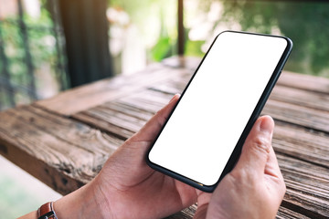 Mockup image of hands holding black mobile phone with blank desktop screen on wooden table