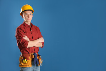 Handsome young working man in hard hat against color background, space for text