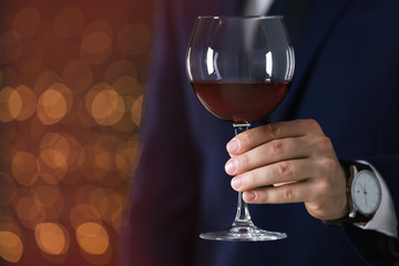 Man in formal suit with glass of wine against blurred background, closeup. Space for text