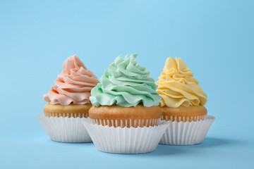 Tasty cupcakes with cream on light blue background