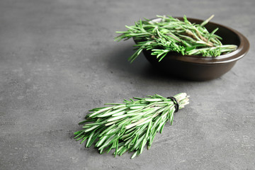 Bunch and bowl with fresh rosemary on grey table