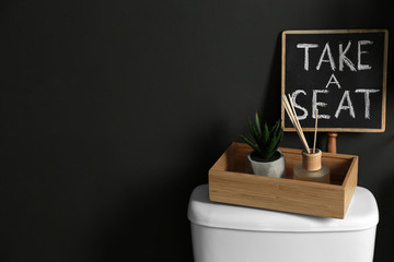 Decor elements and toilet bowl near black wall, space for text. Bathroom interior