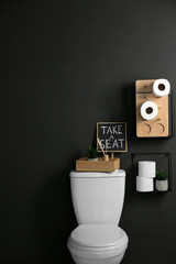 Decor elements, necessities and toilet bowl near black wall, space for text. Bathroom interior