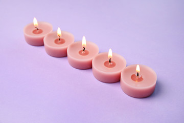 Fototapeta na wymiar Burning wax decorative candles on purple background