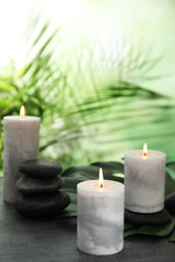 Burning candles and spa stones on grey table against blurred green background, space for text