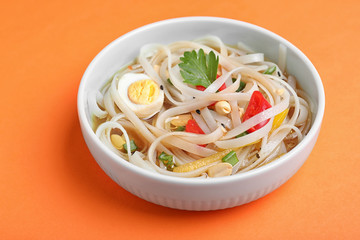 Tasty ramen with rice noodles and vegetables on orange background