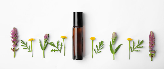 Bottle of essential oil and wildflowers on white background, top view