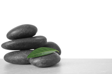 Stack of spa stones and green leaf on table against white background. Space for text