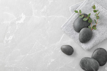 Flat lay composition with spa stones and green leaves on grey table, space for text