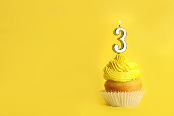 Birthday cupcake with number three candle on yellow background, space for text
