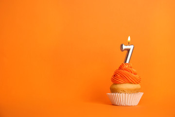 Birthday cupcake with number seven candle on orange background, space for text