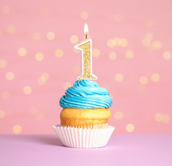 Birthday cupcake with number one candle on table against festive lights