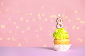 Birthday cupcake with number eight candle on table against festive lights, space for text