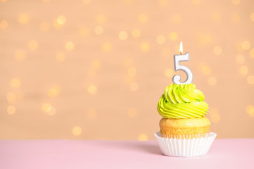 Birthday cupcake with number five candle on table against festive lights, space for text
