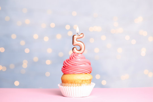 Birthday cupcake with number five candle on table against festive lights