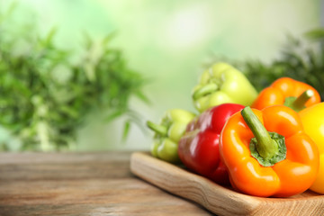 Board with ripe bell peppers on wooden table against blurred background, space for text