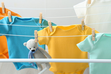 Different cute baby onesies and toy bear hanging on clothes line. Laundry day