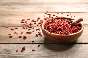 Bowl of dried goji berries and scoop on wooden table, space for text. Healthy superfood