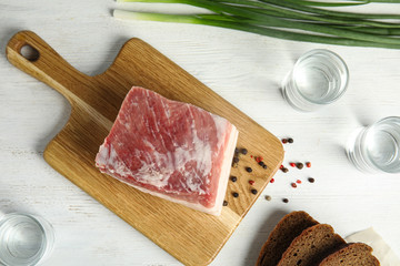Board with pork fatback, onion, bread and shots of vodka on white wooden background, flat lay