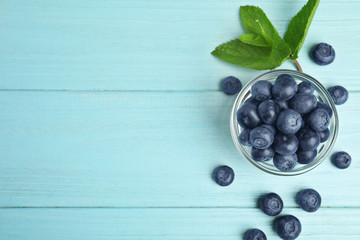 Naklejka na ściany i meble Glass bowl of tasty blueberries and leaves on color wooden table, flat lay. Space for text