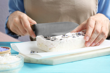 Woman cutting hand made soap bar with lavender flowers at light blue wooden table, closeup