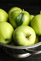 Colander of fresh ripe green apples on black wooden table, closeup view