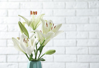 Vase of beautiful lilies against white brick wall, space for text