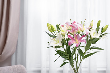 Vase with bouquet of beautiful lilies on blurred background. Space for text