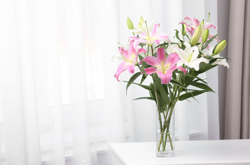Fototapeta na wymiar Vase with bouquet of beautiful lilies on white table indoors. Space for text