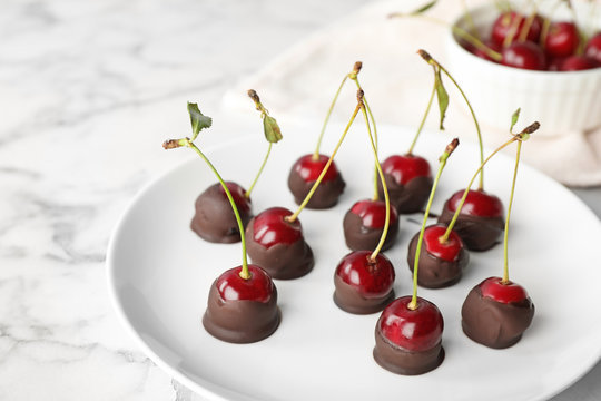 Plate of chocolate dipped cherries on white marble table