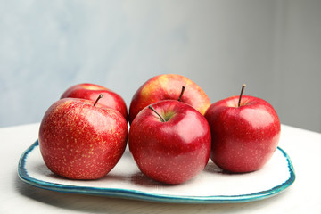 Plate with ripe juicy red apples on white wooden table against grey background