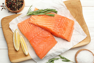 Wooden board with salmon fillet on white table, flat lay