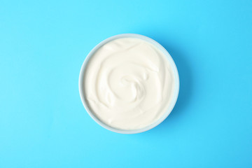 Bowl of sour cream on light blue background, top view
