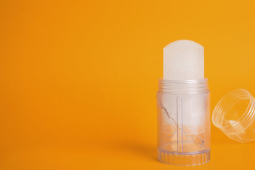 Natural crystal alum stick deodorant and cap on orange background. Space for text