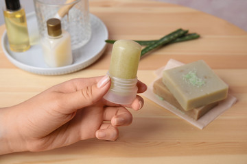 Young woman holding natural crystal alum deodorant at wooden table, closeup