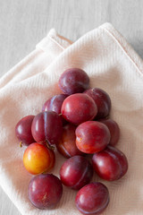 British organic plums, freshly picked, on a pastel pink tea towel. Grey wood background