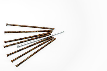 Metal shiny sharp nail in the center of a pile of old rusty nails on a white background.