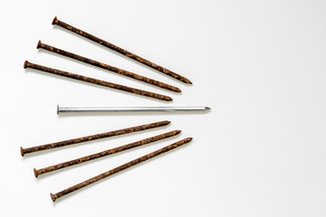 Metal shiny sharp nail in the center of a pile of old rusty nails on a white background.