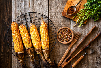 Corn grilled with cheese and spices on the dark rustic background. Autumn food background. Fast food in the summer or fall. Toned image. Flat lay.