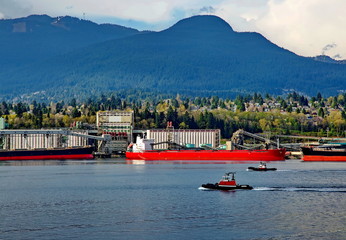 Two tugboats go along the port of North Vancouver against the background of cityscape and mountain range