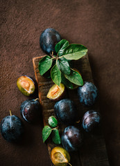 Fresh ripe plums with leaves on a brown wooden board. Top view, toned image. Selective focus.