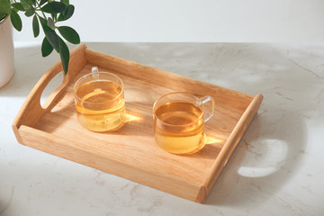 Hot tea is in the glass. Placed on a wooden tray.