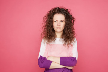 Pretty Caucasian young blue eyed curly haired woman, dressed casually, crossing arms with sceptic...