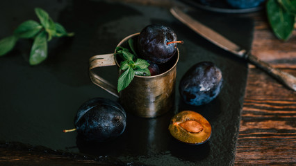 Garden plums in cup on stone plate. Fresh organic fruits. Food background. Healthy food. Toned image. Copy space for your text.